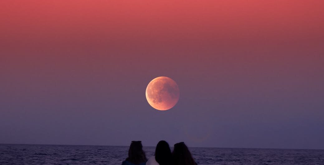 three women sitting on rock infront of ocean