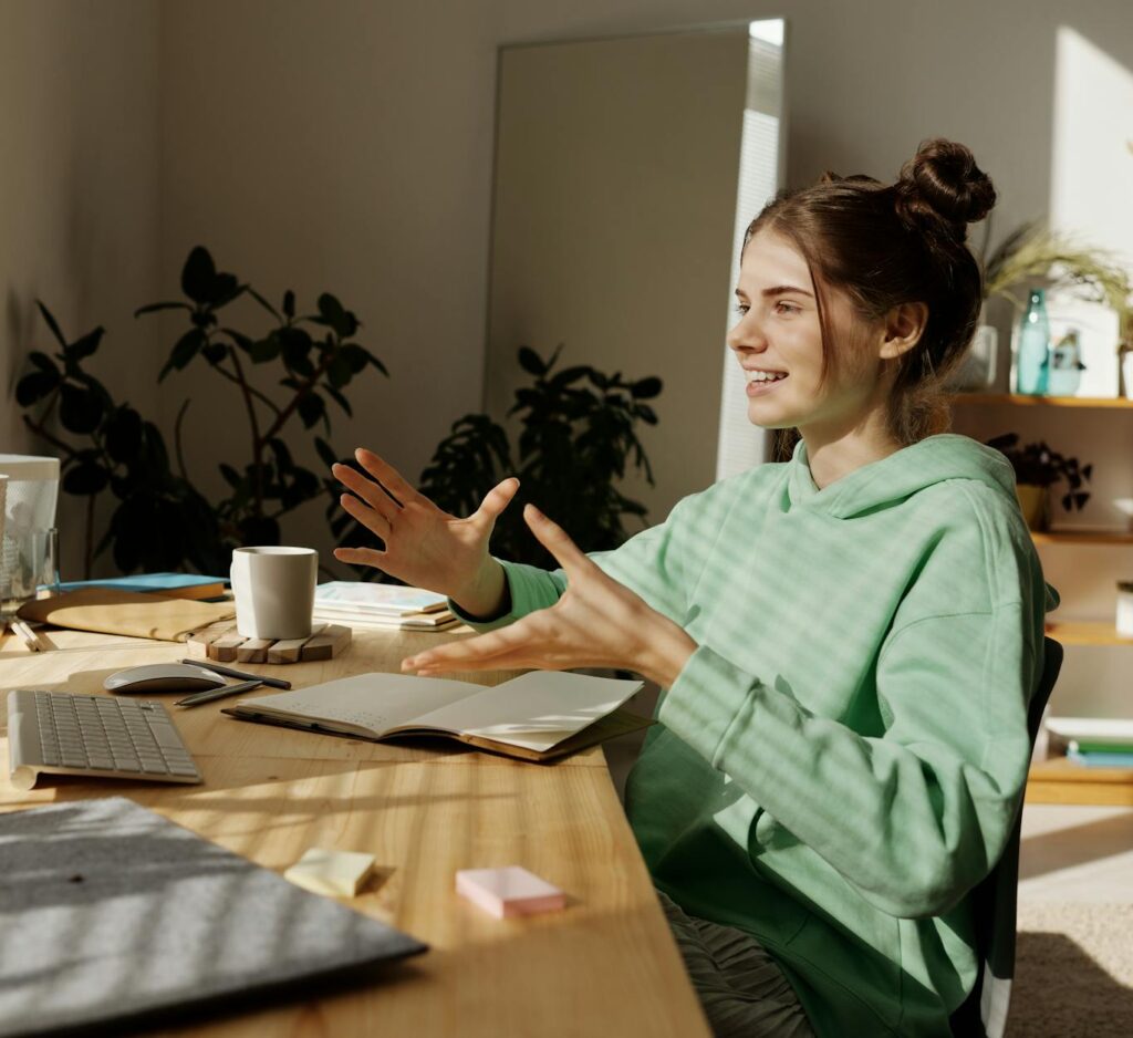 a woman in green hoodie sitting near the table while having conversation through her desktop